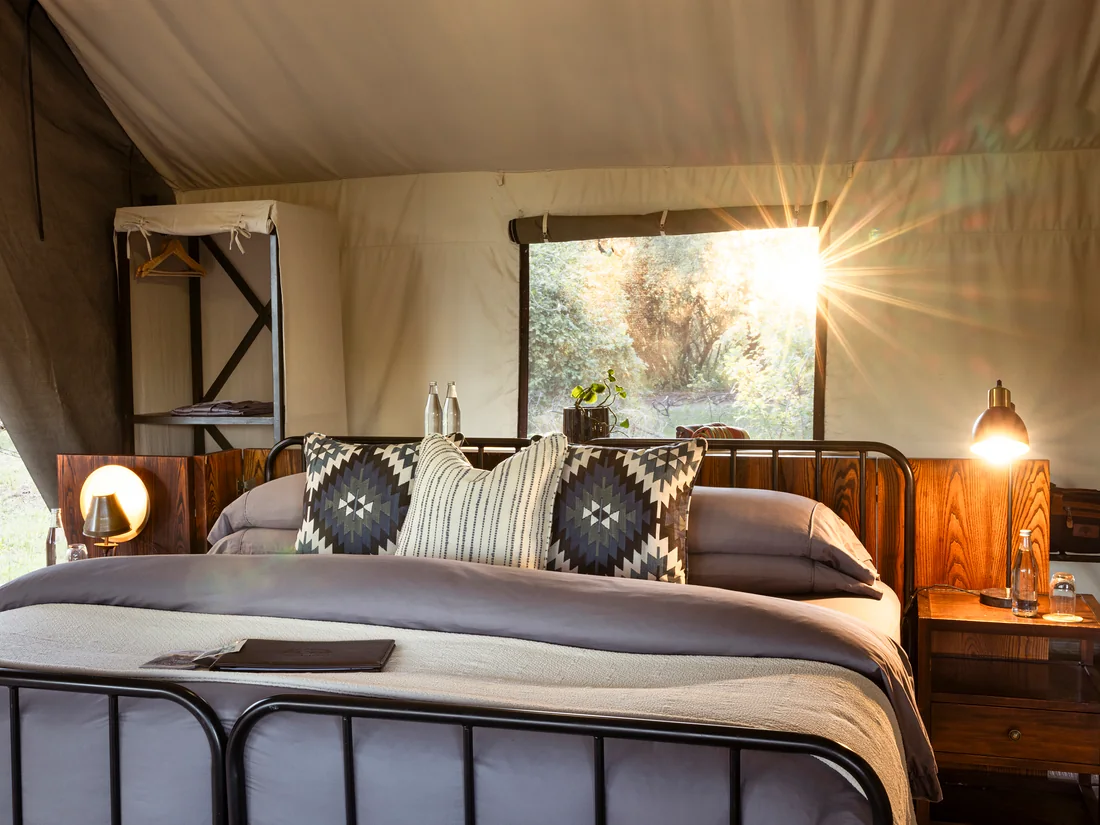 Bed inside a safari tent with a view of the bush