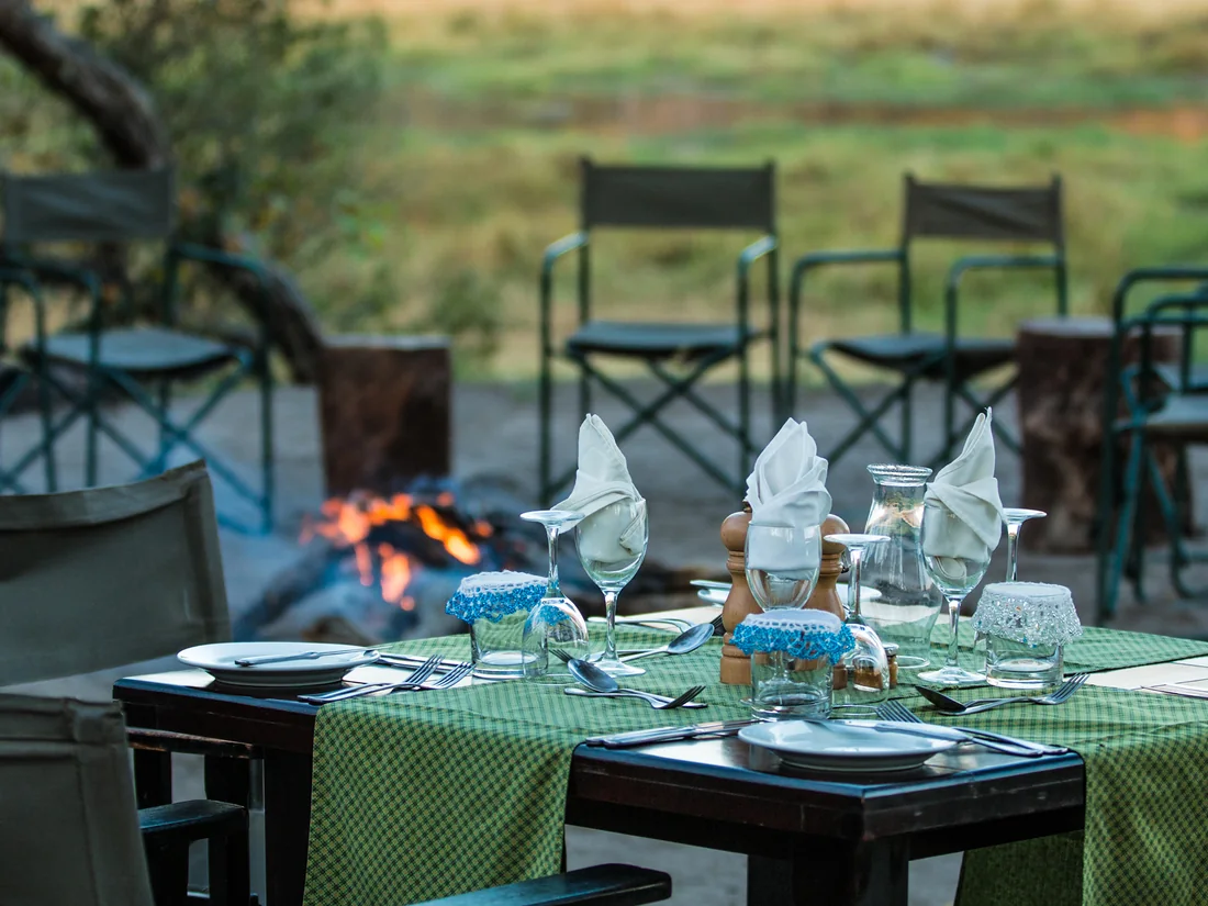 Outdoor dining table set for a meal beside a campfire