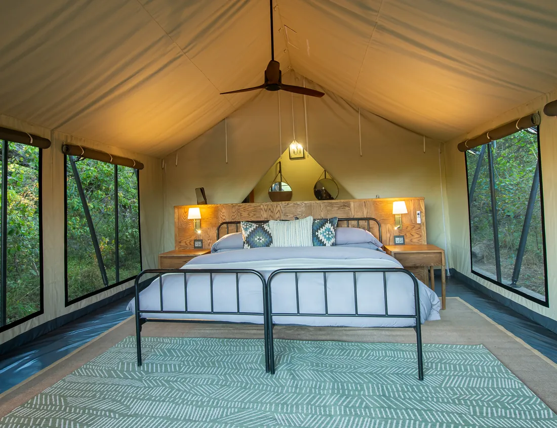 Bed inside a safari tent with forest visible through the windows